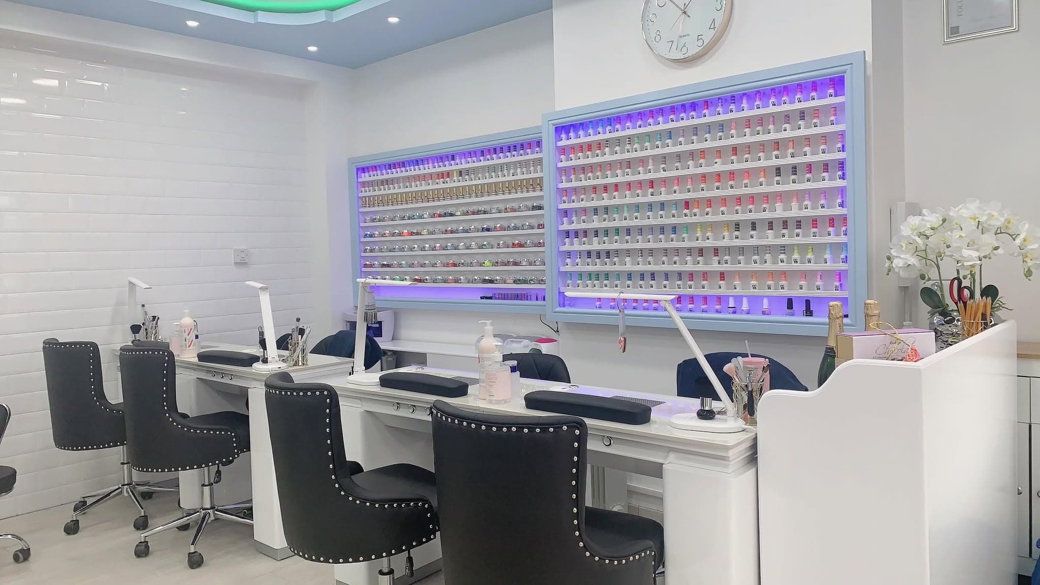 Inside Ly’s Nails on Augusta Street: manicure desks with studded black chairs in front of two lit walls of gel colours